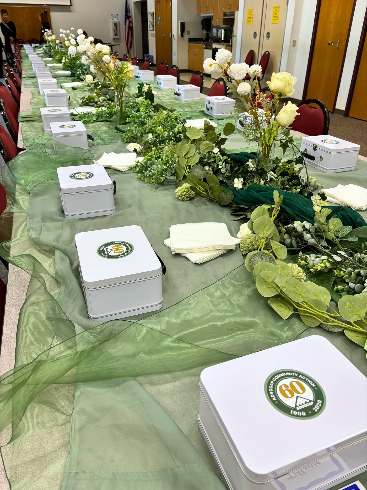 Lunchboxes with ADVOCAP logo sit on table decorated with ADVOCAP colors and flowers.