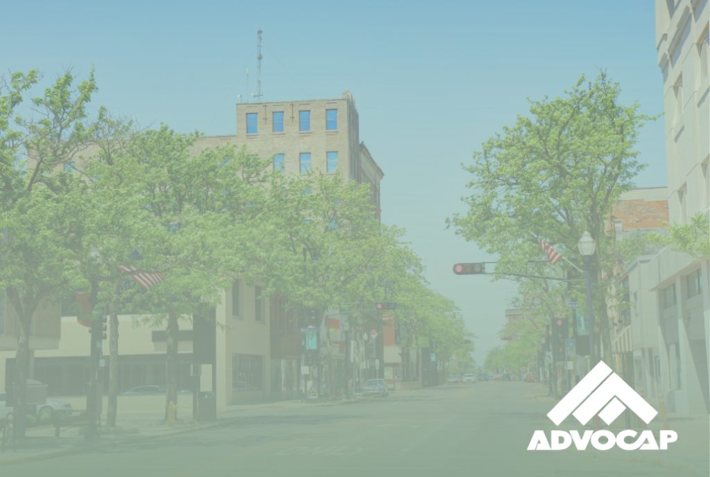 Main Street in Fond du Lac, buildings and street lined with trees. ADVOCAP logo in bottom right corner.